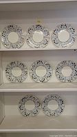 Nine Wedgwood dinner plates displayed on shelves, showing front design with blue, silver, and black floral pattern on white porcelain.