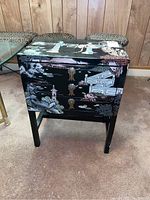 Front view of black Asian cabinet showing detailed inlay artwork with figures and brass drawer pulls.