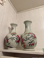 Pair of ceramic vases with painted peach and branch design, standing side by side on a shelf.