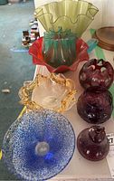 Various colored glass bowls and vases grouped on a white surface, showing the range of shapes and colors.