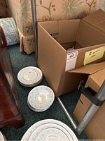 Multiple stacks of bone china plates and cups/saucers beside a cardboard box labeled '8 piece set'. Plates have a blue and silver decorative pattern around rim.