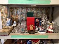 Wide shelf view showing nine Mikasa keepsake boxes, ceramic figurines including angels, glass trees, candleholders, a music box, and other decorative holiday items.