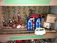 Photo showing multiple Santa figurines, two crystal Santa figurines in boxes, a crystal tree, some mugs, a music box, and other Christmas decorations grouped on a shelf.
