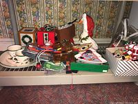 Photo of assorted Christmas figurines and decorations including tissue box covers, holiday boxes, goose wearing Santa hat, and Spode teacup and saucer.