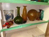 Shelf display showing all items: clear crackle vase with blue accents, green decanter, amber vase, globe, bud vases, stoppers