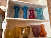 Shelf holding seven crackle glass items including five vases and two pitchers in various colors: blue, red, light blue, amber, and purple.