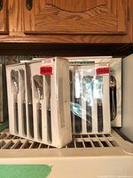 Three boxed sets of Oneida flatware, each containing 5 pieces in original packaging with price stickers visible, plus visible black picnic cutlery bag with strap.