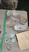 Overview of porcelain dishes including floral-patterned trays, candy dishes, and the silver-tone covered jar with spoon.