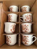 Photo showing 6 ironstone teacups with brown floral design packed in cardboard box compartments.