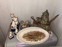 Overview showing all figurines and platters on a table against white wall.