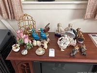 Overview of porcelain figurines including birds, dogs, deer, flowers, and bulls on a wooden surface.