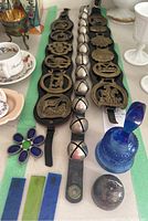 Wide view of horse bridal medallions in brass on leather straps alongside jingle bells and stained glass pieces on table.