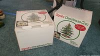 Two closed original boxes of Spode Christmas Tree 16-piece starter sets placed on carpeted floor, showing front and side box details