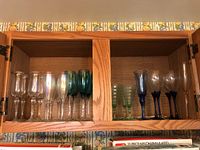 Overall view of cabinet with multiple types of stemware including clear, iridescent, green, and blue glasses