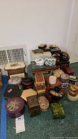 Photo showing a variety of vintage and keepsake trinket boxes of different sizes, shapes, and materials arranged on the floor.