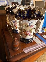 Front view of both ceramic Asian vases on a wooden dresser showing floral decorations and dark blue gold-trimmed scalloped tops.