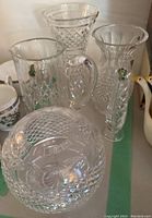 Five pieces of Waterford crystal displayed on a surface, including bubble bowl, pitcher, and three vases.
