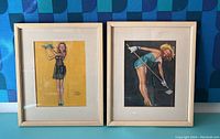 Both framed pin-up drawings side by side in front of patterned backdrop