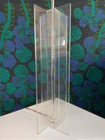 Front view of the lucite table lamp against floral patterned background, showing clear panels and geometric design.