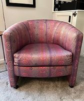 Front view of barrel chair showing pink, purple and orange patterned satiny silk fabric upholstery and plastic castors on legs.