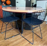 Full view of round dining table with pink and mauve high-gloss laminate top, black solid wood base, shown with black wire chairs for demonstration only.
