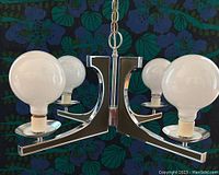 Front and angled view of the 1970s swag light chandelier showing its chrome and greenish black metal arms with four plain round bulbs installed without globes.