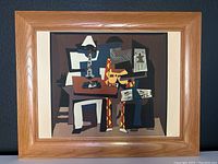 Full view of framed silkscreen print of Picasso's Three Musicians featuring cubist figures in vibrant colors with light oak frame and fabric backing.