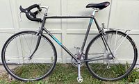 Side profile of vintage 1980s Trek 420 road bike showing dark gray frame, black drop handlebars, and rear carrier, photographed on grass.