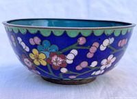 Side view of antique Chinese cloisonné enamel rice bowl showing plum blossom floral design on royal blue background with green scalloped rim.