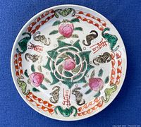 Top down image showing decorative enamel painted peaches, bats and red calligraphy symbols on porcelain plate.