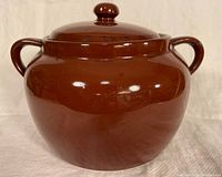 Brown glazed bean pot with lid shown from front, with two loop handles and round knob lid.