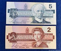 Front side of 1986 Canadian $5 and $2 bills showing portraits and denomination markings.