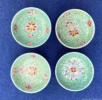 Top view of four small porcelain bowls with turquoise Famille Verte floral enamel decoration showing embossed gold scrolls and pink flowers. One bowl has a different pattern.