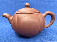 Side view of brownish-red purple sand pottery teapot showing gourd form with rounded lobes, bamboo style handle, spout and knob lid with ventilation holes.
