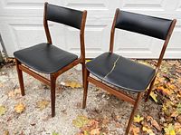 Pair of vintage Danish teak dining chairs with black vinyl seats and backs, showing one seat with a slash and the other chair with a crack in the support leg