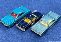Photo of three Husky Models diecast toy cars on blue fabric background: turquoise Cadillac Eldorado with red interior, dark blue police Buick Elantra with yellow details, metallic blue Oldsmobile Starfire Coupe.
