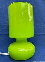 Photo of lime green Ikea LYKTA table lamp on blue background, showing full lamp shape and glossy finish