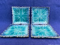 Four vintage Japanese porcelain plates viewed from the top on a blue fabric background showing turquoise to blue gradient glaze with leaf vein pattern and scalloped edges.