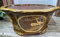 Side view of brown glazed planter showing detailed oriental crane motifs in framed panel on one side
