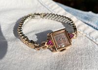 Full angled view of ladies watch showing square face with red stones and expansion band