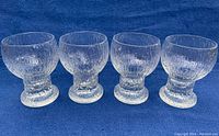 Four clear textured crystal goblets standing in a row on blue fabric background.