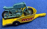 Photo of metallic pale green die cast Honda motorcycle placed on yellow trailer marked with 'HONDA' in red letters.