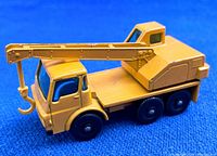 Side view of yellow die cast Dodge crane truck showing the crane arm extended and plastic hook, black wheels, and truck cab details on a blue background.
