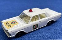Front left angle view of white Matchbox Ford Galaxie die cast police car showing roof red light, police shield decal on hood and door, and clear plastic windows.