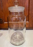 Front view of a vintage clear glass apothecary jar with a round glass stopper lid, marked British Made S 11 on base.