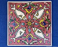 Top view of one vintage ceramic tile with four white fish and colorful floral pattern on reddish background.