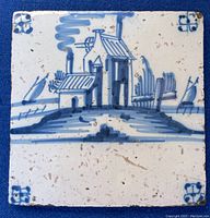 Front of vintage Delft tile showing hand painted blue and white house and sailboats design with corner decoration.