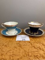 Two Aynsley corset-shaped teacups with matching saucers, one cobalt blue and one light blue, on wood surface.