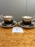 Two Royal Albert Regal Series teacups with matching saucers on wood surface, showing full set