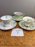 Photo showing all three teacups and saucers arranged on a wooden surface, highlighting the green color tones and style differences.